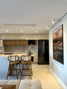 Cozinha integrada com ilha de pedra, marcenaria em madeira e bancos, em apartamento reformado em São Paulo. Projeto LUVIN, obra Siolam Engenharia