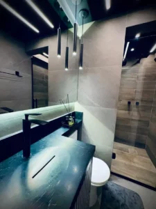 Banheiro de apartamento reformado em São Paulo com bancada de pedra escura, pendentes pretos e revestimento amadeirado - Siolam Engenharia