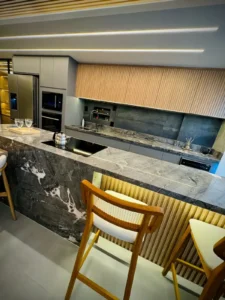 Cozinha gourmet reformada em apartamento com bancada de pedra natural, ripado de madeira e iluminação embutida - Siolam Engenharia