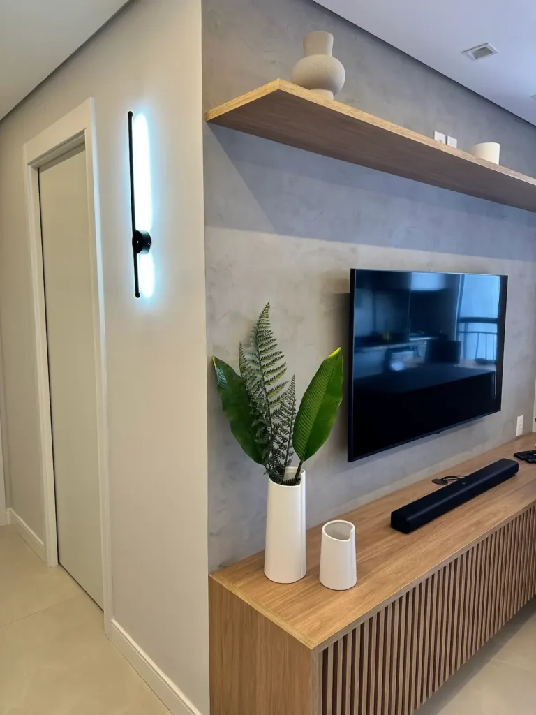 Sala de estar reformada com parede em cimento queimado, prateleira e painel ripado de madeira - obra da Siolam Engenharia